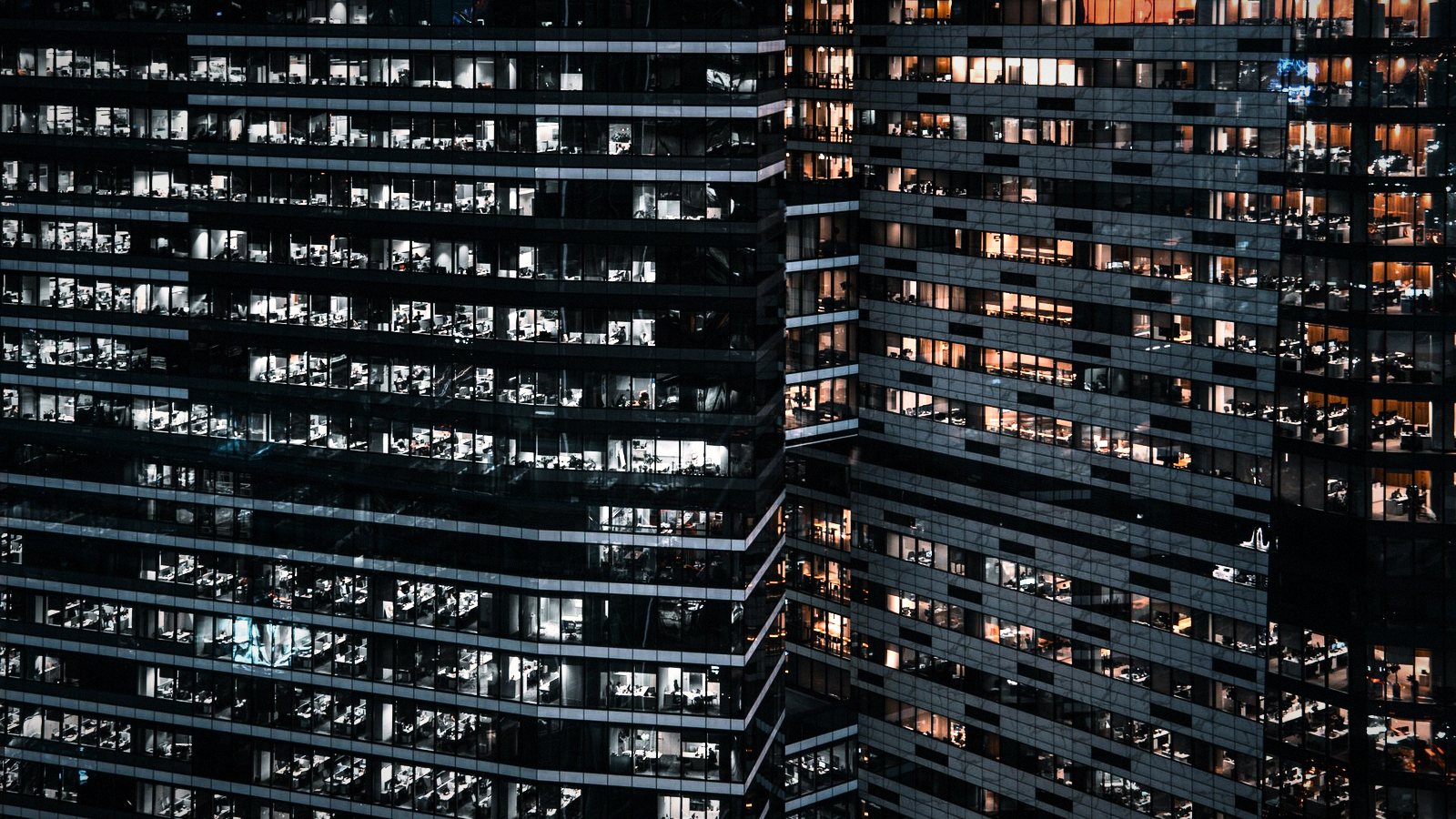 Glass residential towers at dusk, apartment windows lit in a grid